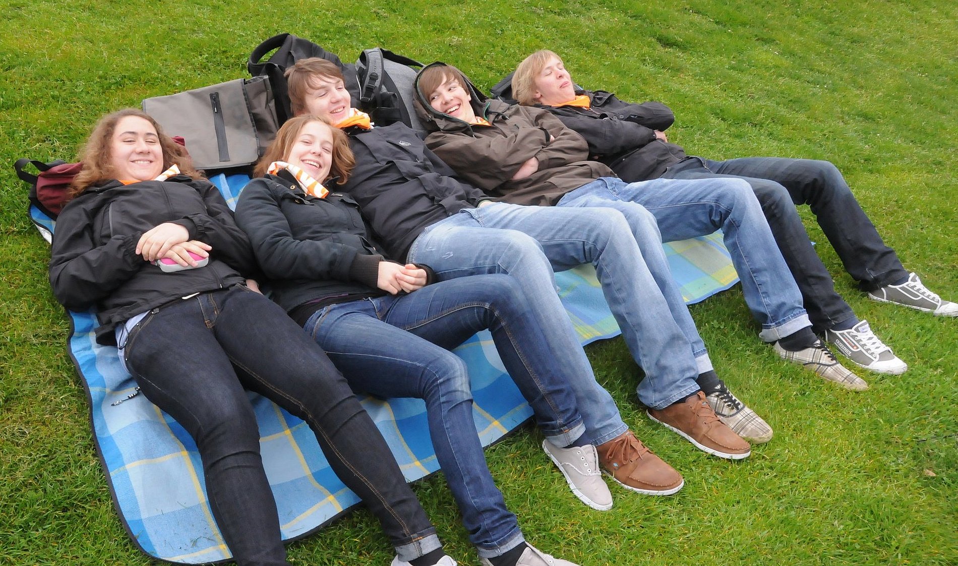 Das Bild zeigt Jugendliche, die auf einer Decke, auf einer Wiese liegen. 