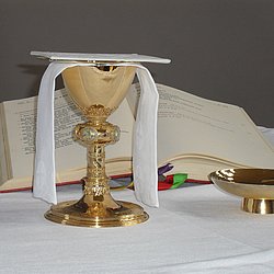 Das Bild zeigt eine aufgeschlagene Bibel, die auf einem Altar liegt. Davor stehen eine Weinkelch und eine Hostienschale. 